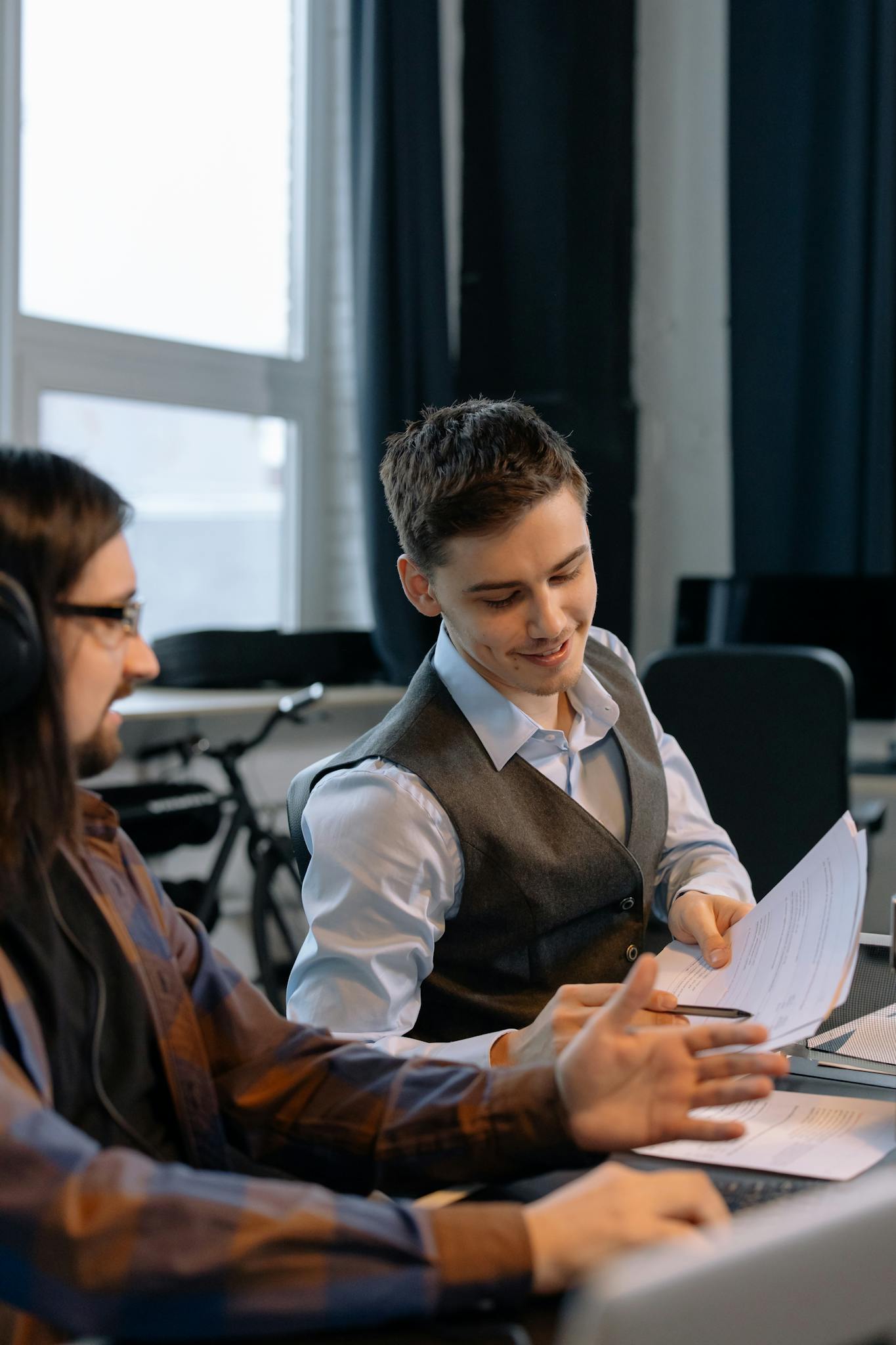 Two young men collaborating with documents in a modern office setting, emphasizing teamwork and productivity.